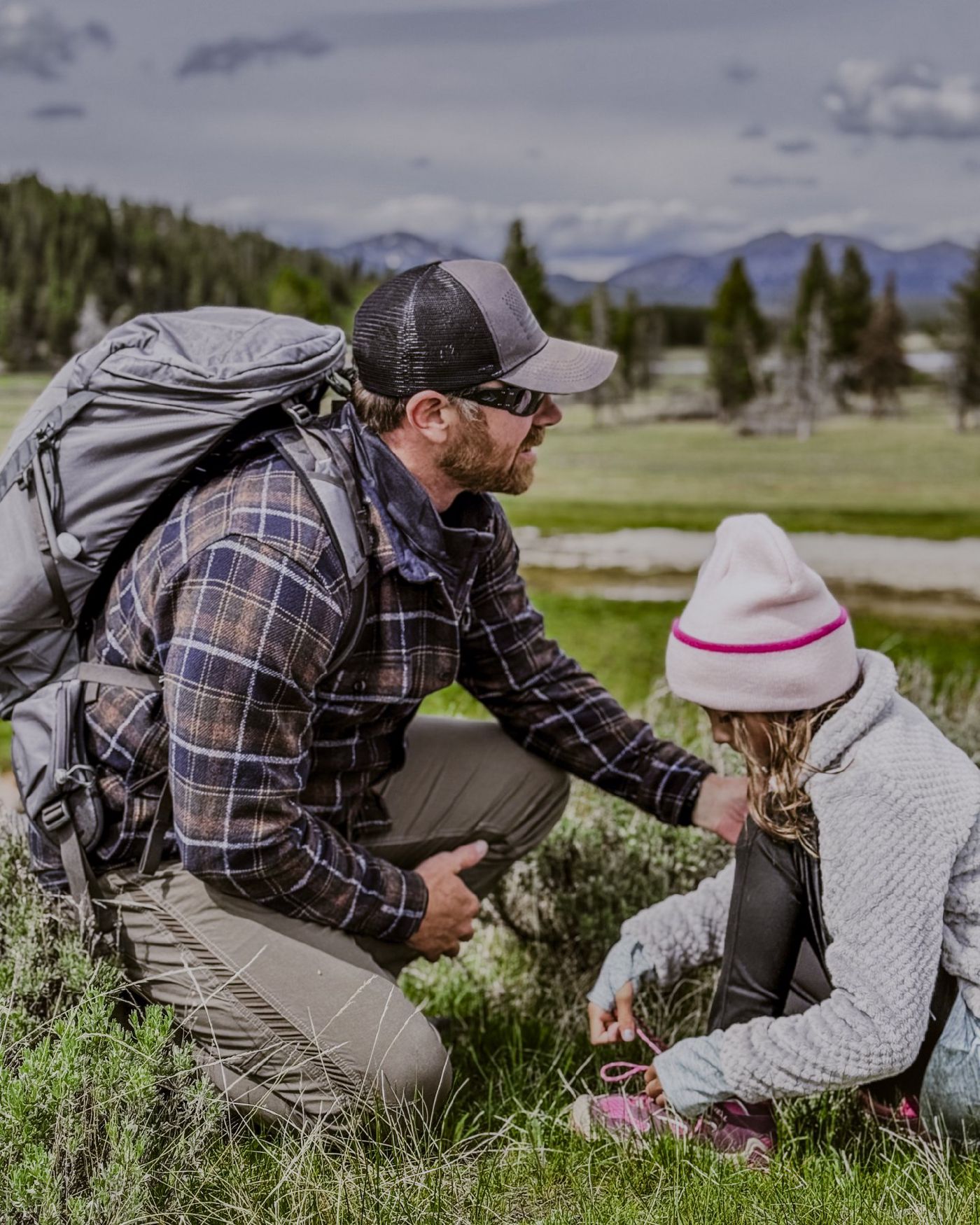 Bryce Henson kneeling beside his daughter in a mountain meadow