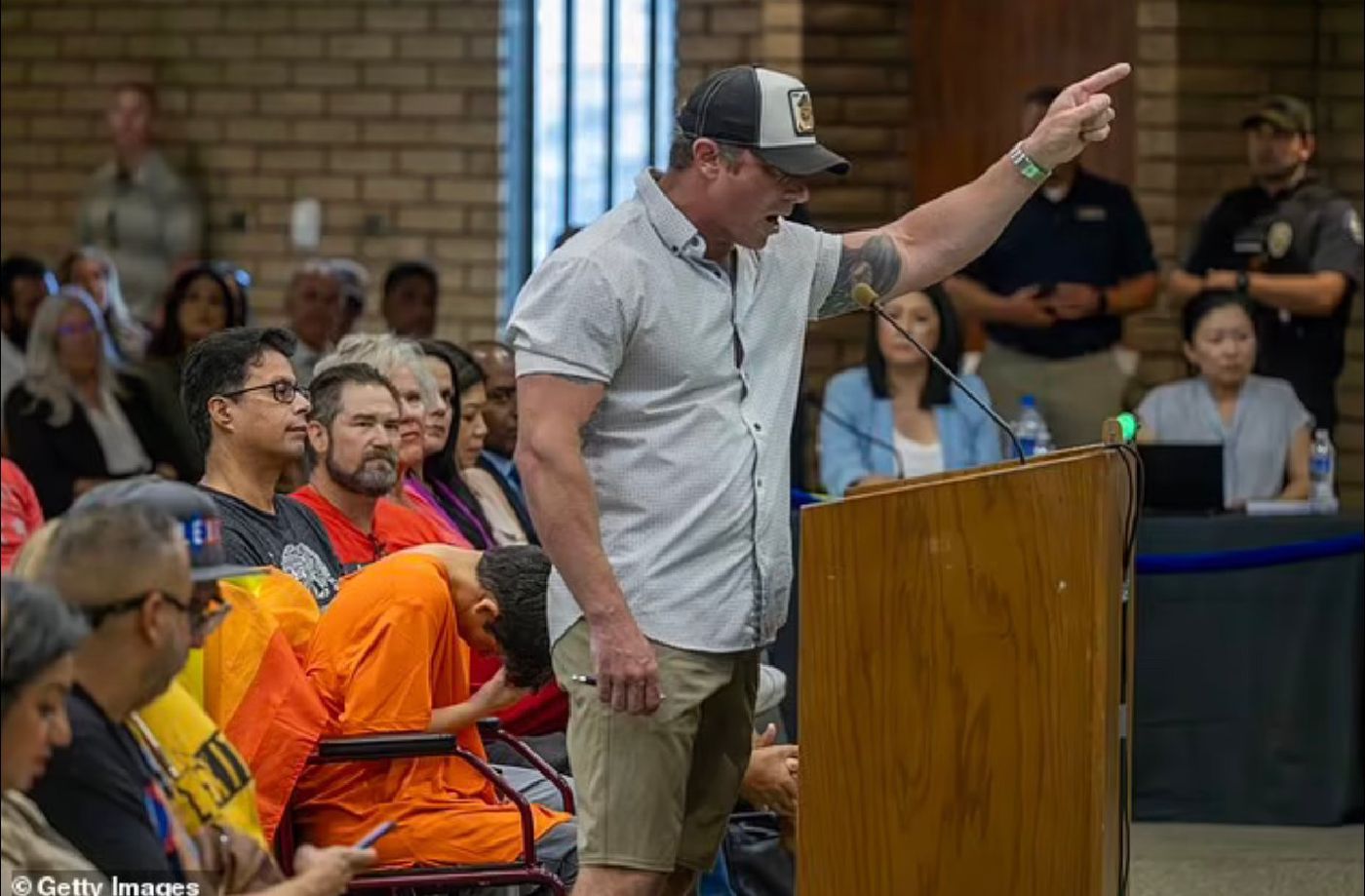 Bryce Henson speaking at a podium during a packed school board meeting